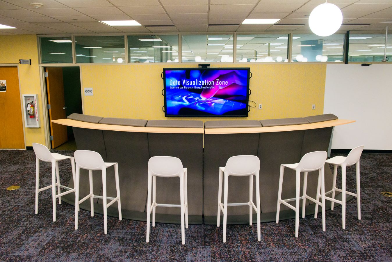 The Data Visualization Zone screen in front of high top chairs in the Dragons' Learning Den